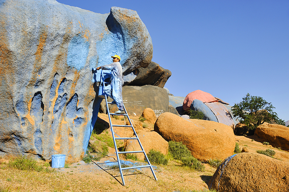 Painter working on Painting Rocks site, work of the Belgian artist Jean Verame. around Tafraout,Anti-Atlas,Morocco,North Africa