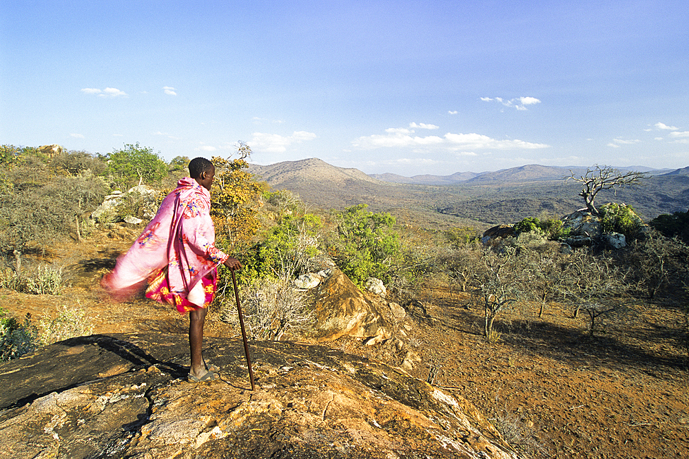 Maasai man standing on the top of a rock looking at the landscape, in the area around Namanga,Kenya, East Africa