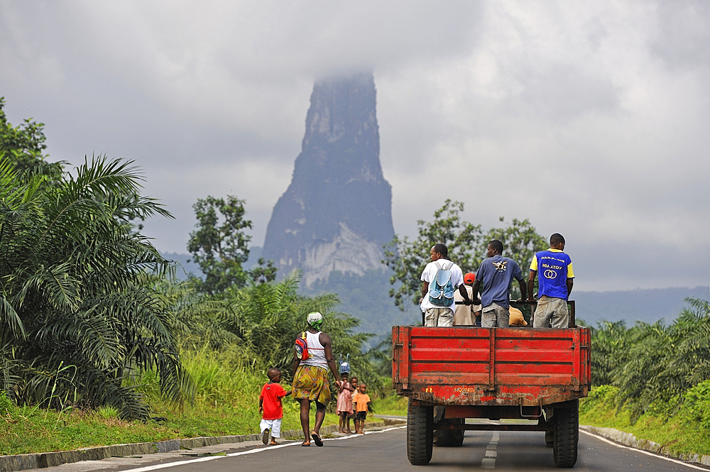Woman and child walking on southern road as a truck is passing, with the Pico Cao Grande (Great Dog Peak) in the background,southern part of Sao Tome Island, Republic of Sao Tome and Principe,Africa