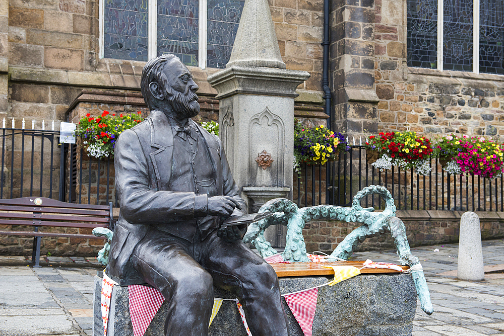 Bronze statue of Victor Hugo sitting on a granite bench, by the artist Mark Cook, in front of the Town Church, St Peter Port, Guernsey Island, Bailiwick of Guernsey, United Kingdom