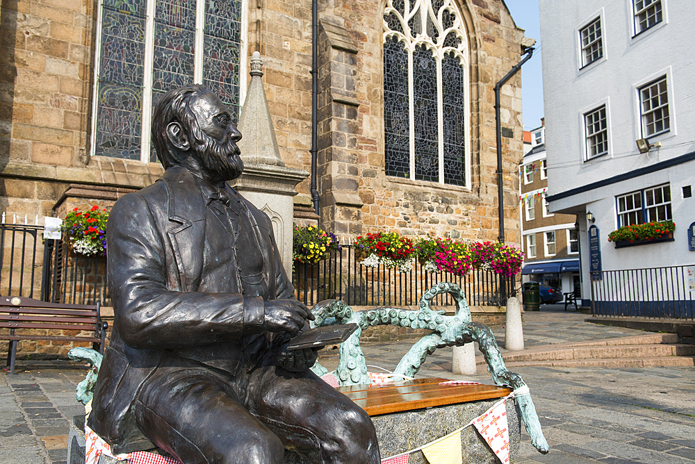 Bronze statue of Victor Hugo sitting on a granite bench, by the artist Mark Cook, in front of the Town Church, St Peter Port, Guernsey Island, Bailiwick of Guernsey, United Kingdom