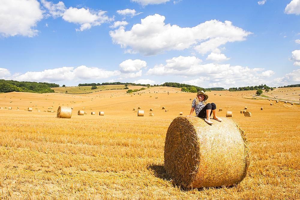 Young girl sitting on a straw roll in an harvested field, Allier department, Auvergne-Rhone-Alpes regionFrance, Europe