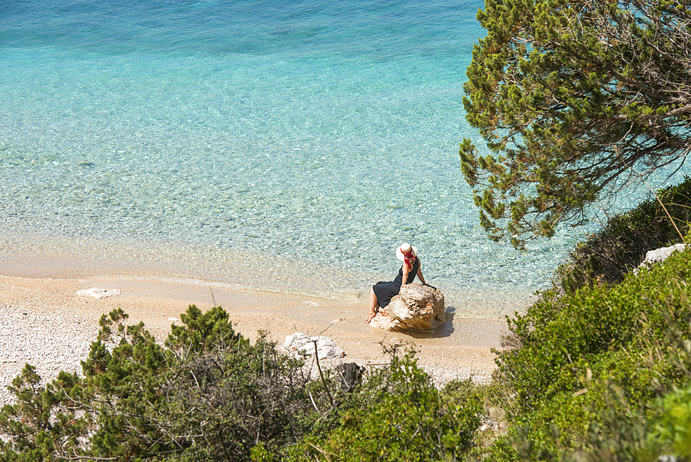 Woman sitting on a rock at the Beach of Dafines Bay, Peninsula of Karaburun, within the Karaburun-Sazan Marine Parc, Vlore Bay, Albania, Europe