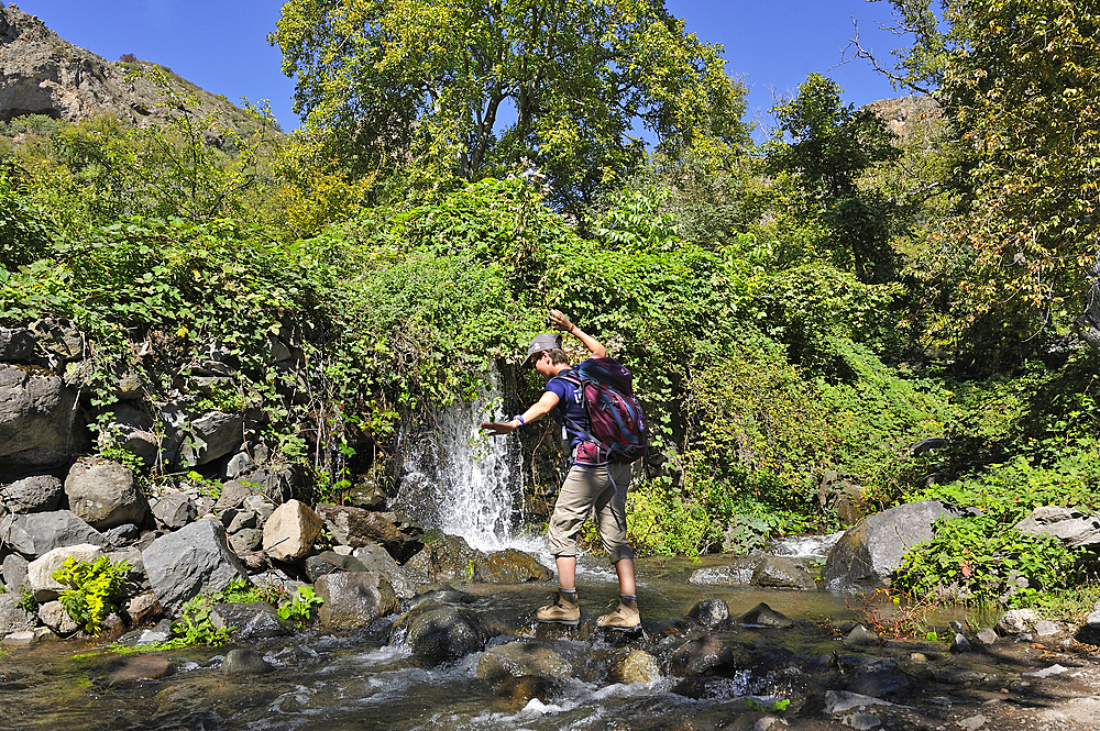 Hiker fording a stream near the deserted village of Old Shinuhayr in the Gorges of the Vorotan River, Syunik region, Armenia, Eurasia