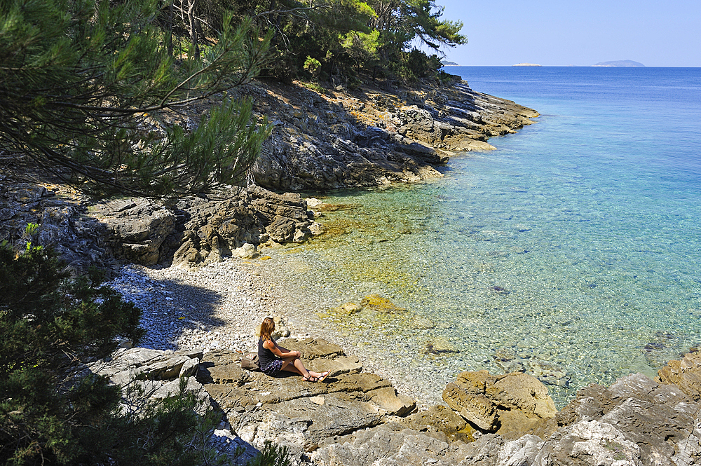 Woman sitting on rocks at a creek of Mrcara islet at the north-west of Lastovo island, Croatia, Southeast Europe