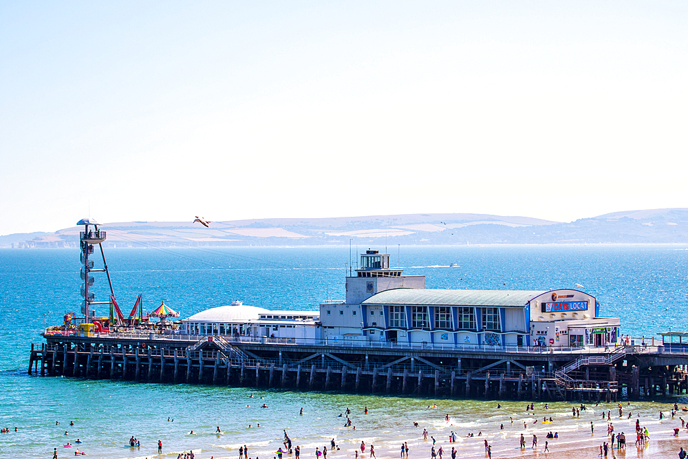 Sunny beach scene with a pier extending into the sea, people enjoying the sand and water, clear blue sky in the background in Bournemouth, Dorset, England, United Kingdom, Europe