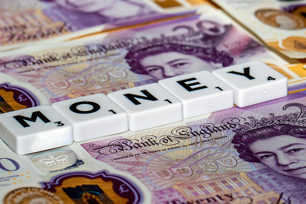 Scrabble tiles spelling MONEY are placed on a background of British 20 pound notes, showcasing the concept of wealth and finance.