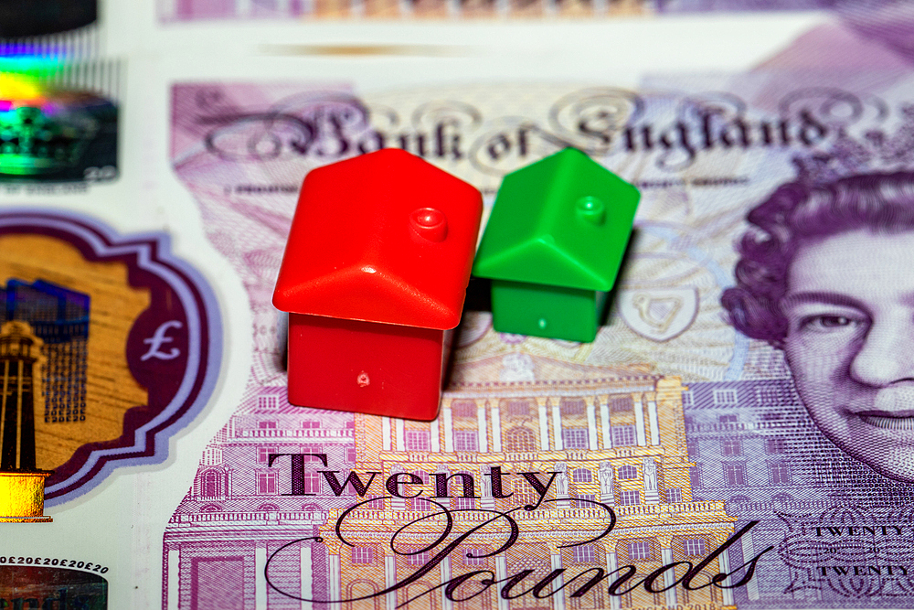 Two toy houses, one red and one green, sit atop a British twentypound banknote featuring a portrait of Queen Elizabeth II.