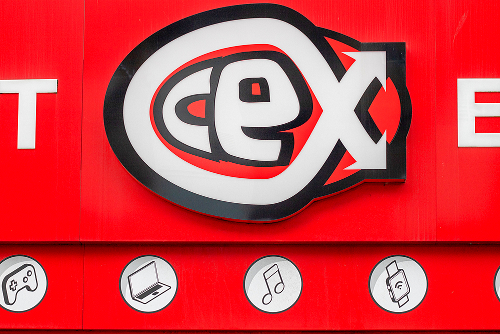 A close-up of a red storefront sign featuring the logo of a retail company. The logo consists of stylized letters 'c', 'e', and 'x' in black and white, with a bold red background. Below the logo are circular icons representing various electronic devices a