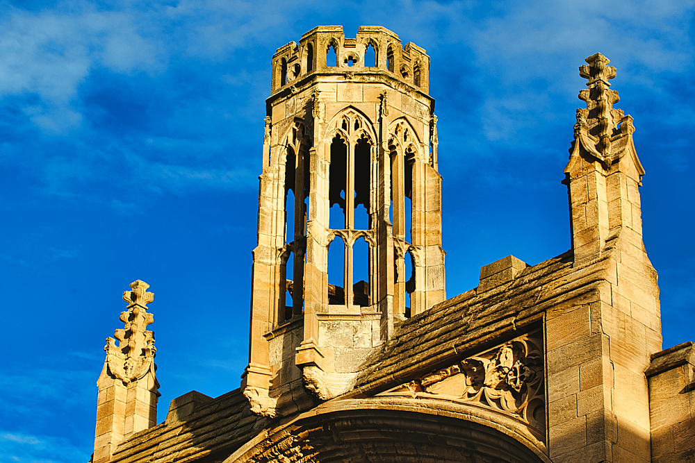 A low angle view of an ancient stone building with an octagonal tower and decorative spires. The sky is a vibrant blue.