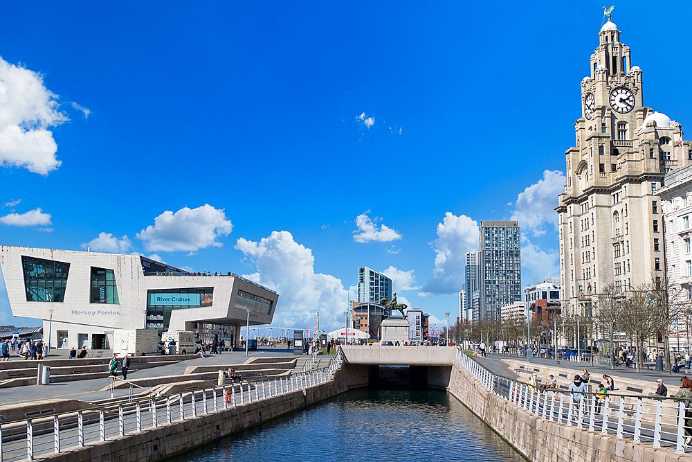 View of Liverpool waterfront featuring the Royal Liver Building, a modern museum, and a canal under a blue sky with scattered clouds.