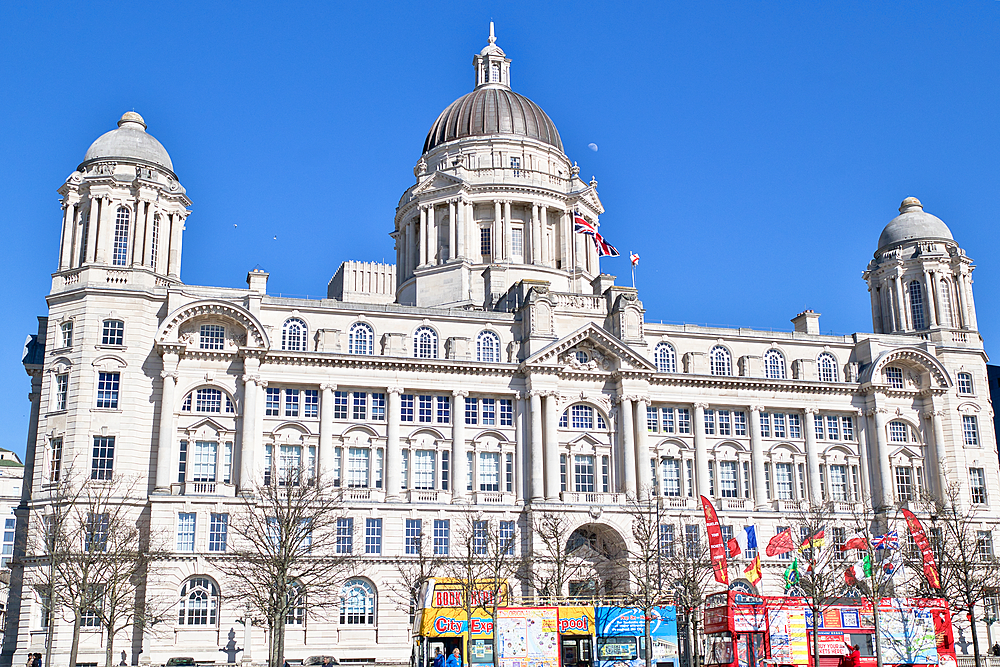 The image shows the Royal Liver Building in Liverpool, a large, ornate building with a clear blue sky as the background. Tour buses are in the foreground.