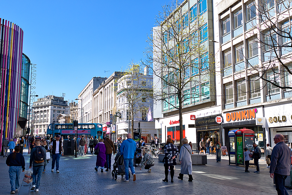 Street scene with pedestrians walking along a commercial street. Buildings flank both sides, and a blue sky is above in Liverpool, UK.