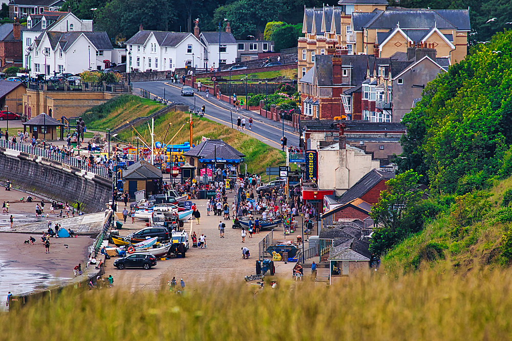 Elevated view of a crowded beach and seaside town with buildings, trees, and beachgoers in Filey, UK.