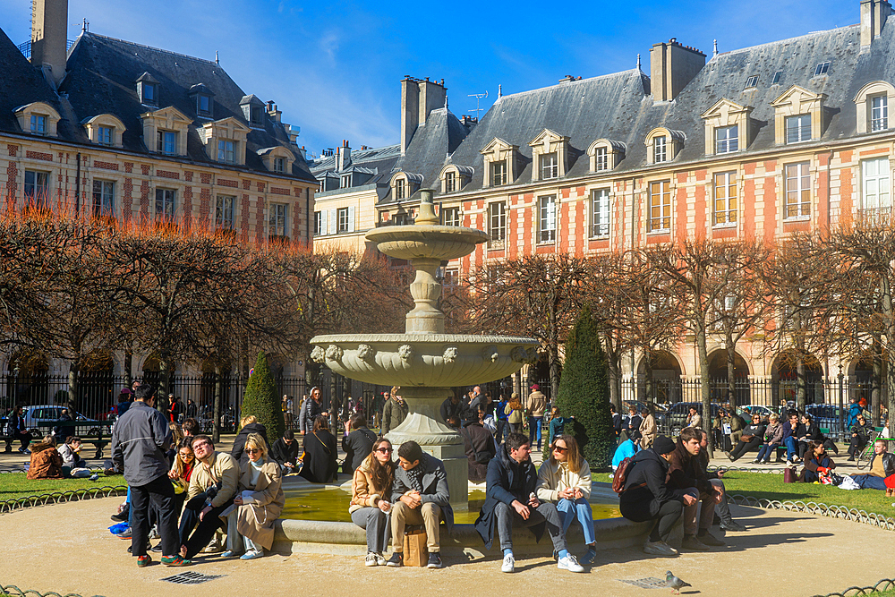People sitting by a fountain in Place des Vosges on a sunny day in winter