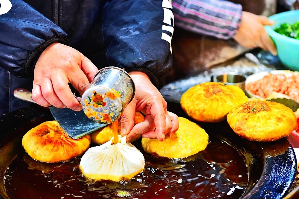 Filling a dumpling with egg batter as it is fried. Song Yuan market, Quzhou City, Zhejiang Province, China.
