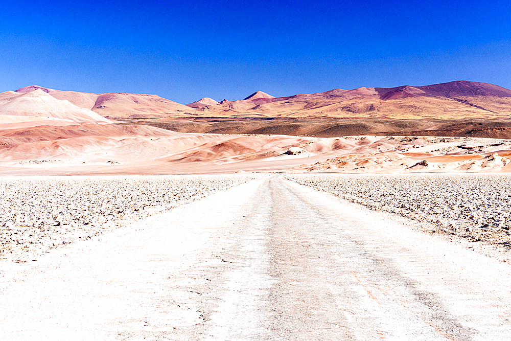 Empty desert road towards red rocky mountains, Salar de Arizaro salt flat, Puna, Argentina