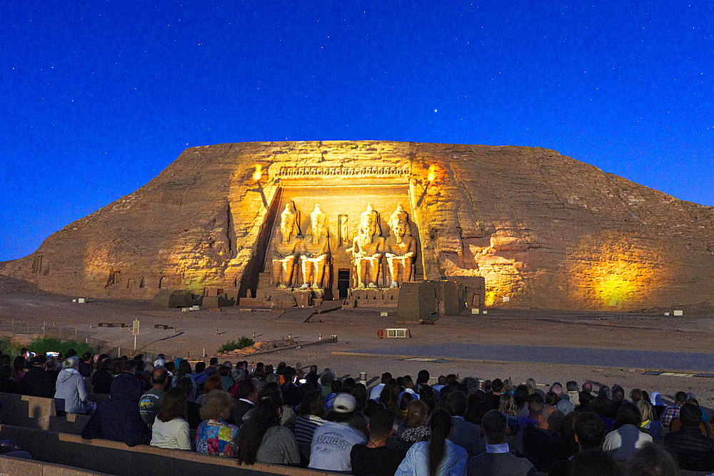 Group of tourists enjoying a sounds and lights performance illuminating the temple of Ramses II at dusk, Abu Simbel, Aswan, Egypt