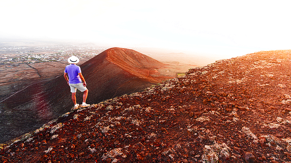 Rear view of man with casual clothing and hat watching sunset on Calderon Hondo volcano, Fuerteventura, Canary Islands, Spain