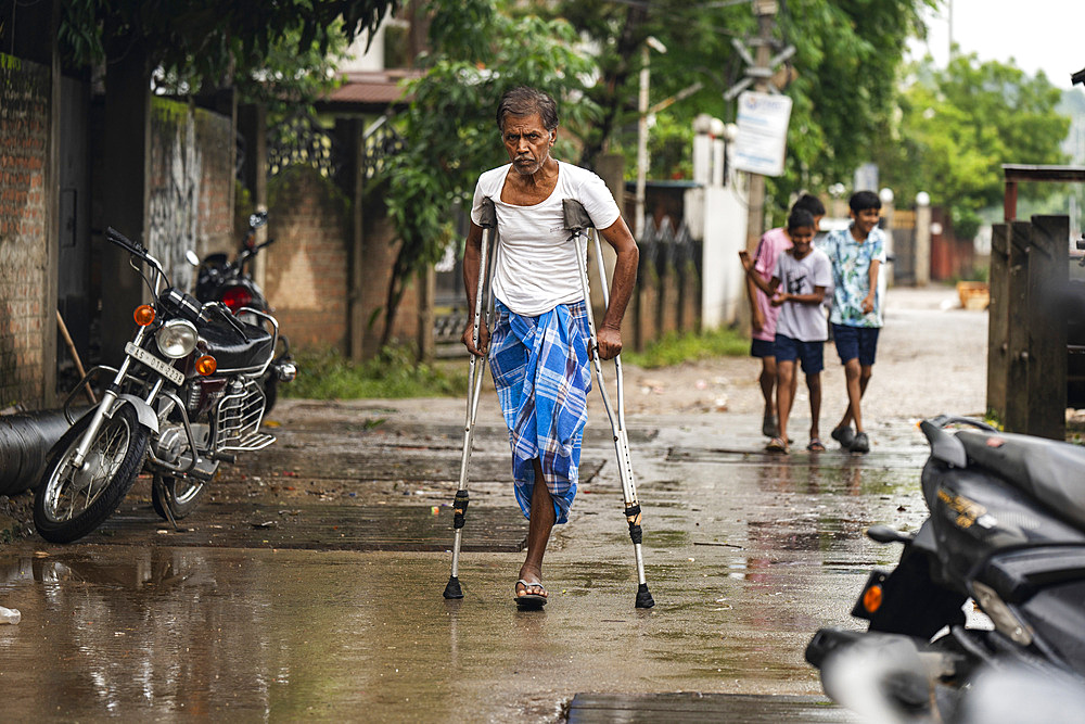 A man with a crutch walking a road