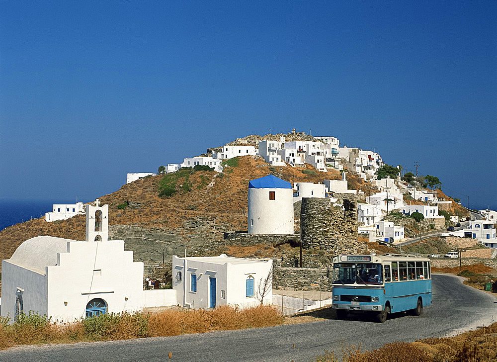 Local bus passing church and white walled village on a hill called The Kastro, on Sifnos, Cyclades, Greek Islands, Greece, Europe