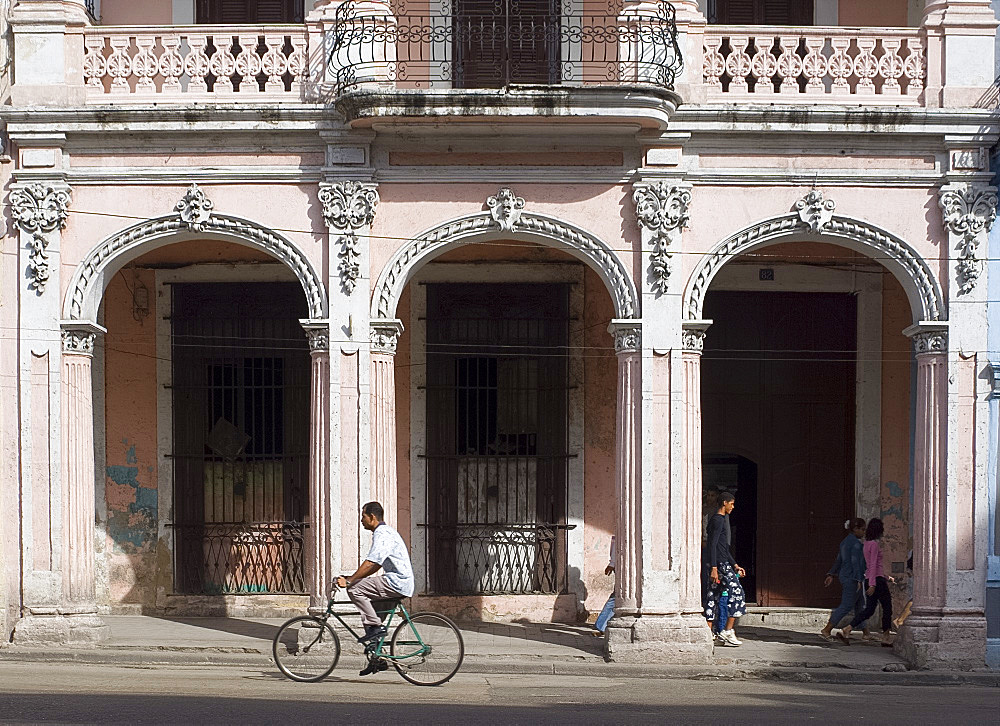 A cyclist passing an ornate old building on Avenida Reina in central Havana, Cuba, West Indies, Central America