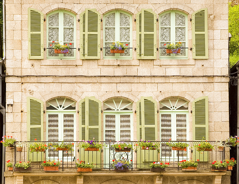 Colourful green wooden shutters and flower covered balcony on old stone building in Dinan, Brittany, France, Europe