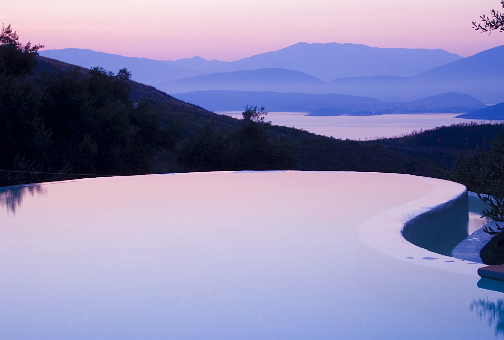 An infinity pool reflecting the sky at sunrise and the mountains of Albania across the Ionian Sea from Ayios Stefanos, Corfu, Ionian Islands, Greek Islands, Greece, Europe