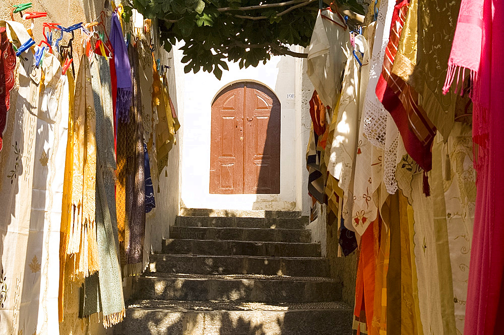 Colourful textiles for sale along steps approaching the Acropolis, Lindos, Rhodes, Dodecanese, Greek Islands, Greece, Europe