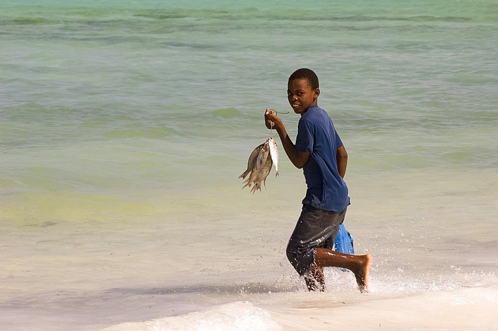 A boy running in the sea with his recently caught fish in hand, Jambiani, Zanzibar, Tanzania, East Africa, Africa