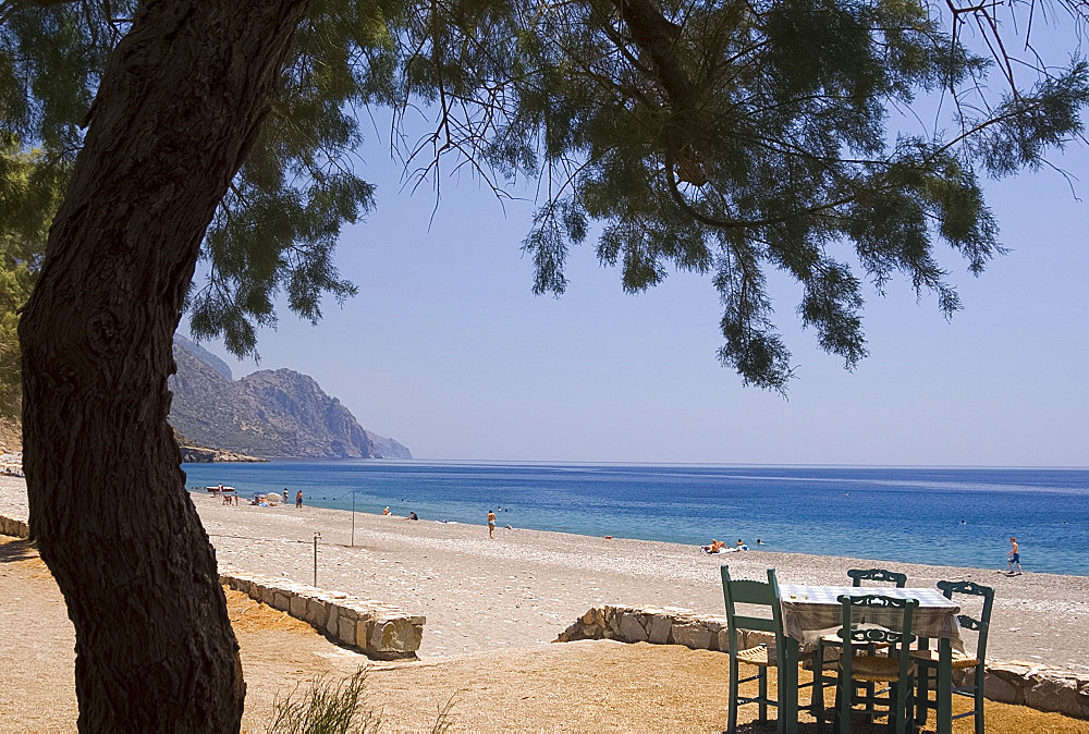 A taverna table facing the sea and pebble beach in Sougia on the south coast of Crete, Greece, Europe