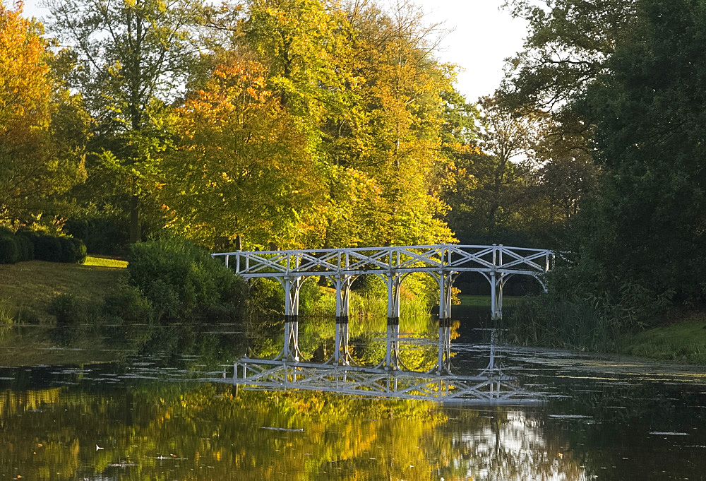 A wooden bridge across the lake at Painshill Landscape Garden in autumn, Cobham, Surrey, England, United Kingdom, Europe