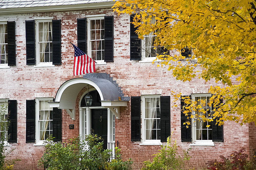 An old brick house displaying an American flag and surrounded by autumn foliage in Townshend, Vermont, New England, United States of America, North America