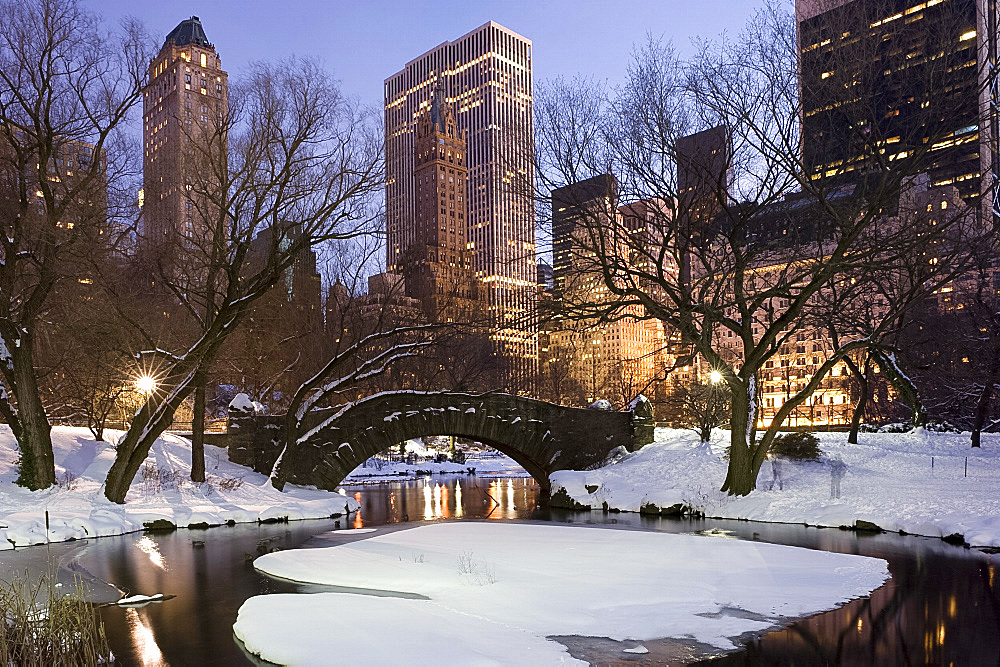 The Gapstow Bridge in Central Park after a snowstorm with skyscrapers behind at dusk, New York City, New York State, USA