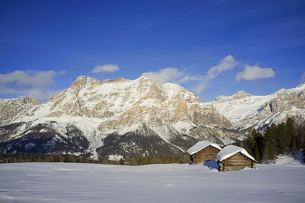 Mounts Lavarella and Conturines behind a pair of snow covered wooden barns at the Alta Badia ski resort near Corvara, Dolomites, South Tyrol, Italy, Europe