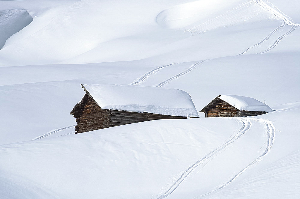 Two old wooden barns surrounded by deep snow and ski tracks in the Dolomites, South Tyrol, Italy, Europe