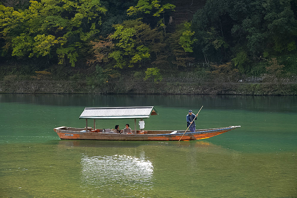 Tourists sightseeing in a small wooden boat on the Oi River in the Arashimaya region outside Kyoto, Japan, Asia