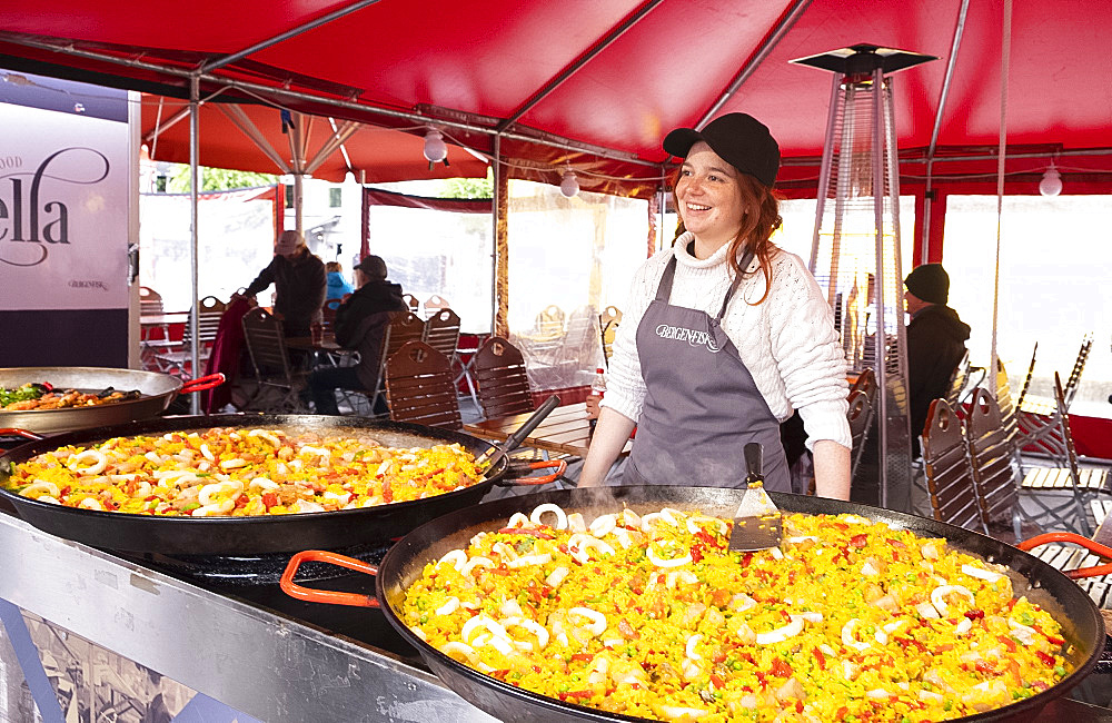 A smiling woman selling paella from huge pans in the fish market in Bryggen, Bergen, Norway, Scandinavia, Europe