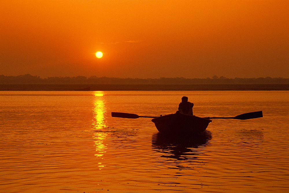 Figure in rowing boat silhouetted at sunset, River Ganges, Varanasi (Benares), Uttar Pradesh state, India, Asia