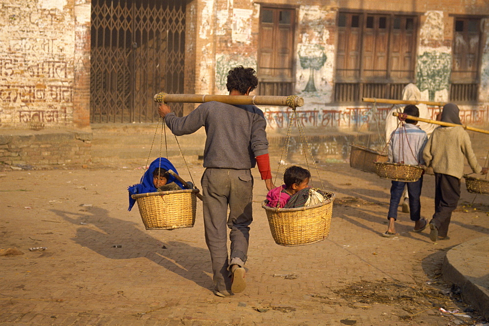 Kids taxi, two children carried in baskets on a pole carried by a man in Bhaktapur, Nepal, Asia