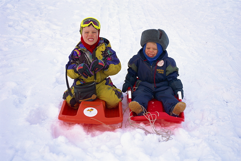 Two children on red toboggans playing in the snow in Finland, Scandinavia, Europe