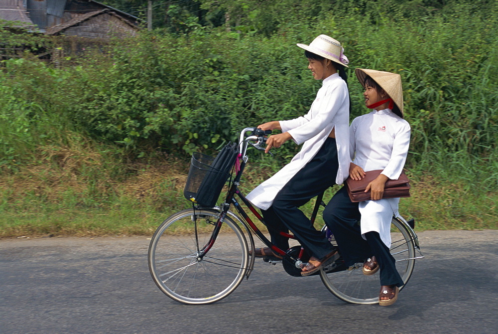 Two school girls in traditional Ao Dai on a bicycle in the Mekong Delta region south of Ho Chi Minh City in Vietnam, Indochina, Southeast Asia, Asia