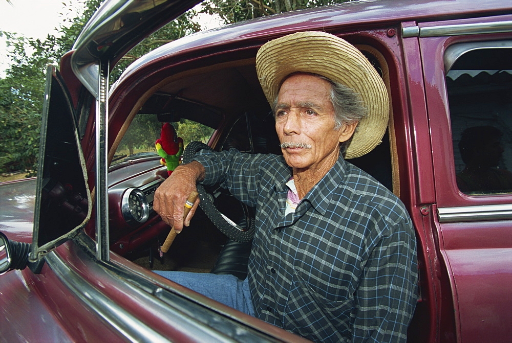 A man sitting in a 1950's American car, Pinar Del Rio Province, Cuba, West Indies, Caribbean, Central America