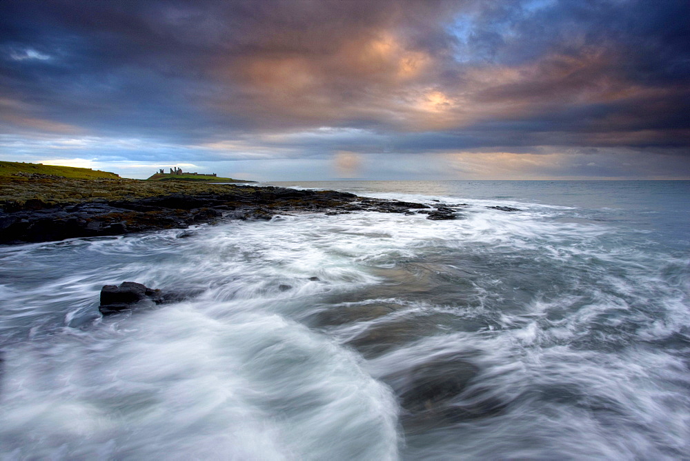 View along coastline on a stormy day towards the ruins of Dunstanburgh Castle, Northumberland, England, United Kingdom