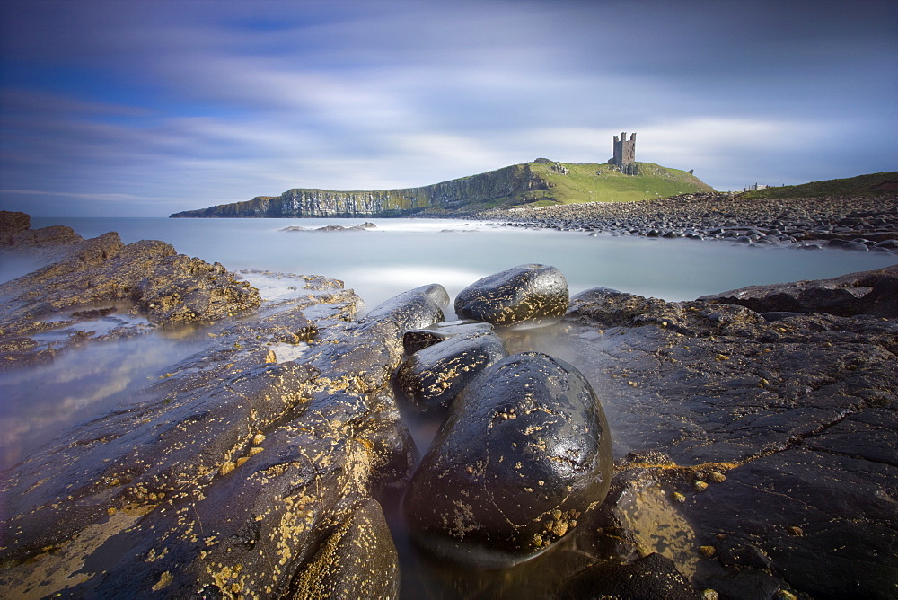 Dunstanburgh Castle bathed in afternoon sunlight with rocky coastline in foreground, Embleton Bay, near Alnwick, Northumberland, England, United Kingdom, Europe