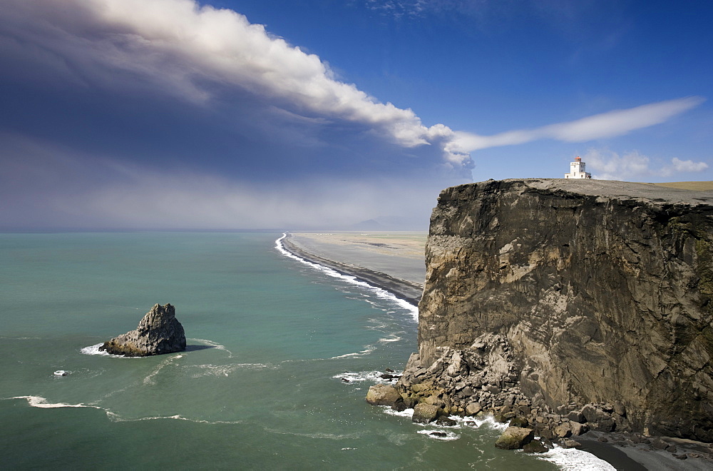 Headland with lighthouse at Dyrholaey looking towards a black volcanic sand beach stretching 15 miles into the distance and the ash plume of the Eyjafjallajokull eruption, near Vik i Myrdal, southern area, Iceland, Polar Regions