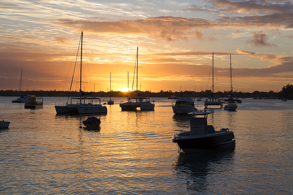 Sunset over the Indian Ocean with boats in silhouette on the calm water off the beach at Gran Baie on the north coast of Mauritius, Indian Ocean, Africa