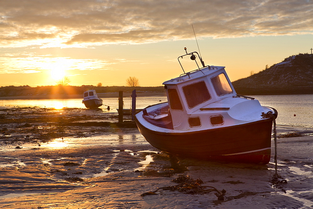 View towards the Aln Estuary during a stunning winter sunrise from the beach at low tide with a fishing boat in the foreground, Alnmouth, near Alnwick, Northumberland, England, United Kingdom, Europe