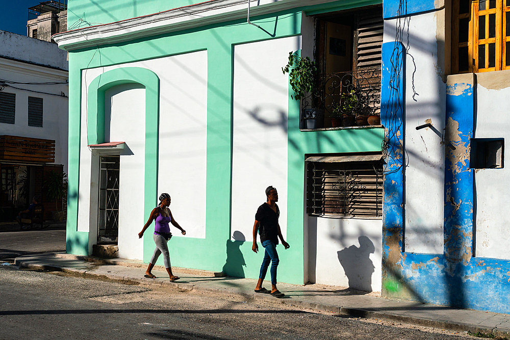 Man and woman (and their shadows) walking through colouful buildings, Old Havana, Cuba