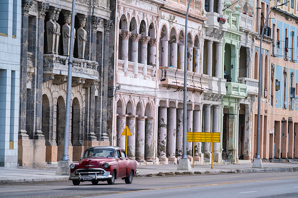 Faded grandeur, stucco, weather-beaten houses on seafront Malecon, with red classic car, Havana, Cuba